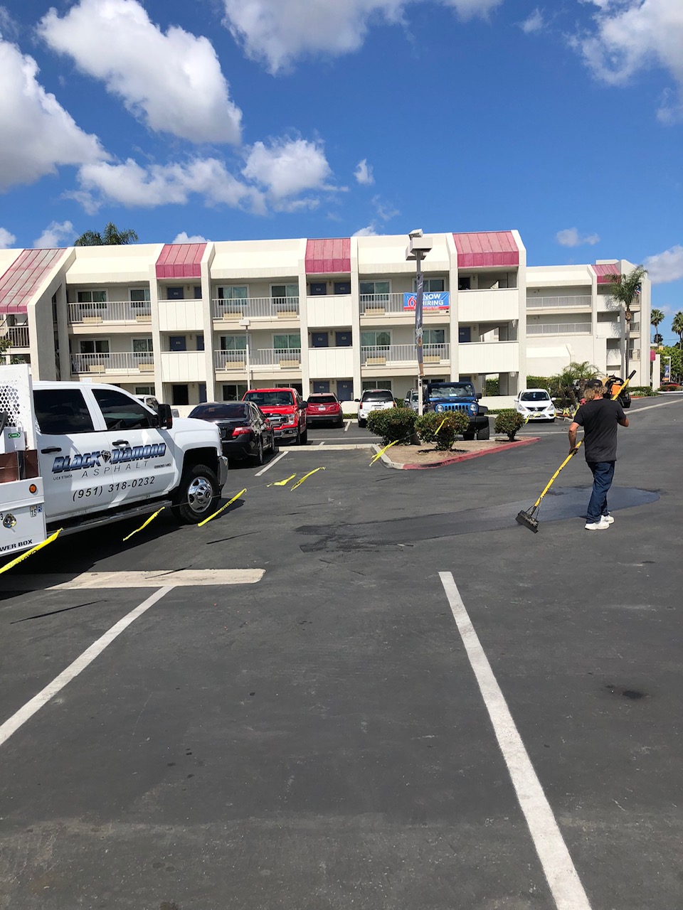 Maintenance technician squeegeeing blacktop sealcoat onto a hotel parking lot with a Black Diamond Asphalt work truck nearby.