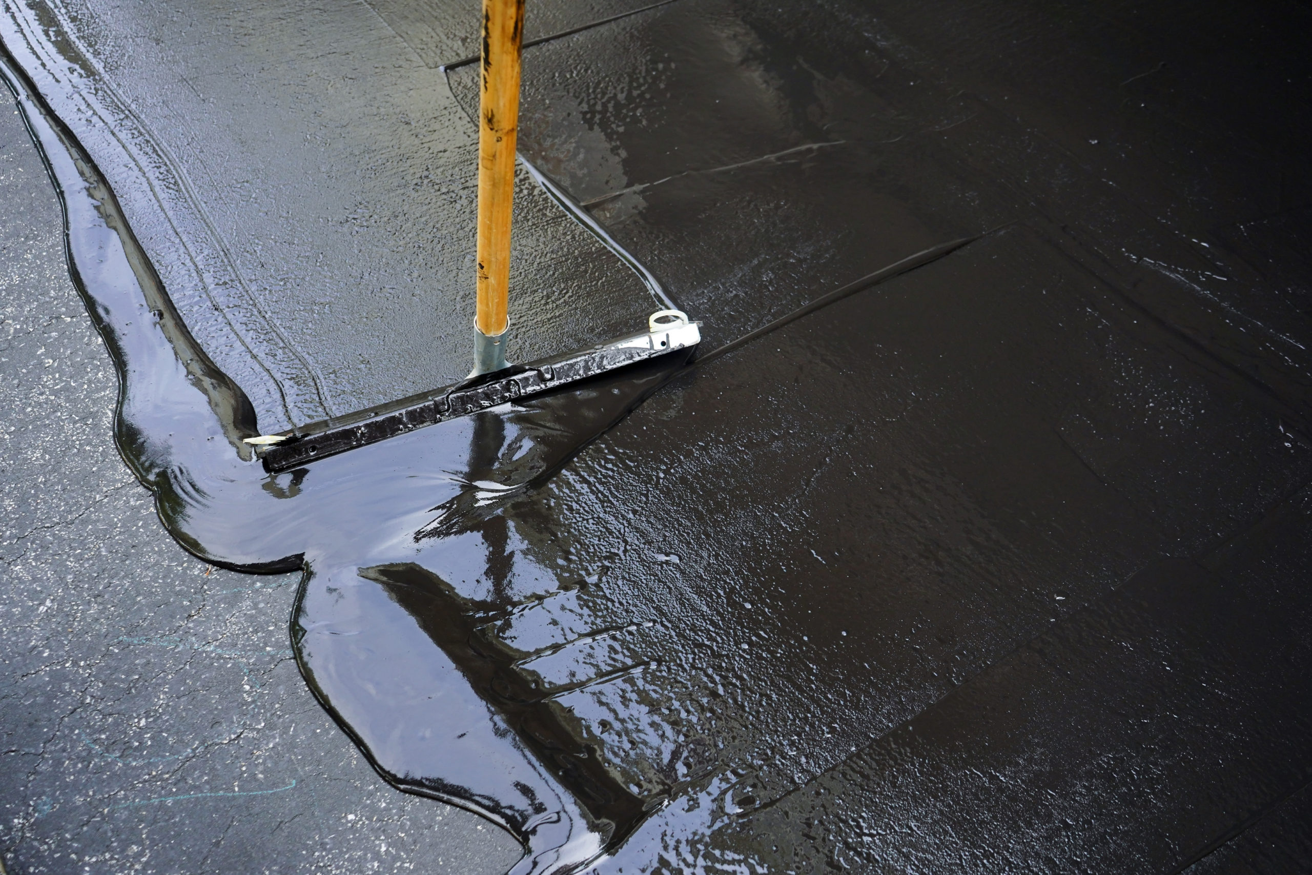 Protective asphalt sealcoating application to prevent oil and sun damage on a residential driveway in Perris.
